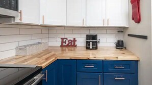 Une cuisine avec des meubles blancs, un plan de travail en bois, une machine à café et un mixeur.