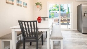 Un coin repas avec une table blanche, des chaises noires et un banc. On peut voir un vase rouge sur la table et une plante suspendue au mur.