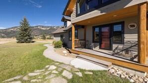 A two-story house with a wooden deck and a stone pathway leading to the entrance. - Twin Antler Retreat | Big Sky | Gallatin River (Gallatin Gateway)
