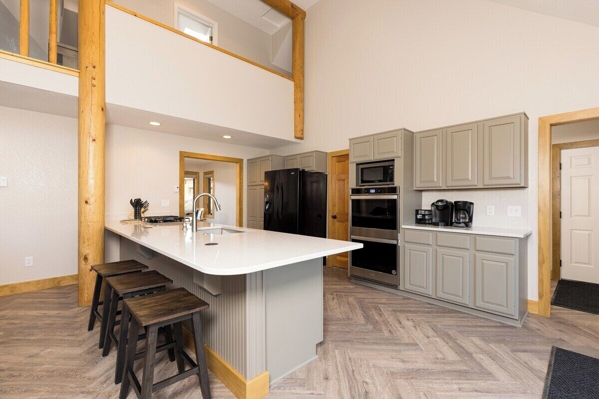 A modern kitchen with a central island, bar stools, a refrigerator, an oven, and a microwave.