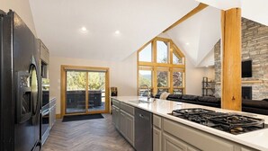A modern kitchen with a large island, built-in appliances, and a stone accent wall. - Twin Antler Retreat | Big Sky | Gallatin River (Gallatin Gateway)