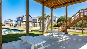 A covered patio area with picnic tables, a pool, and houses in the background.