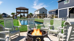 A backyard with a fire pit, outdoor seating, a pool, and a gazebo.