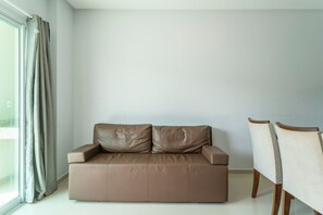 Un salon moderne avec un canapé en cuir marron, deux fauteuils en bois et une grande fenêtre avec des rideaux.