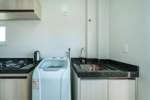 Une cuisine équipée d’une cuisinière à gaz, d’un lave-linge, d’un évier et de meubles de rangement en bois.