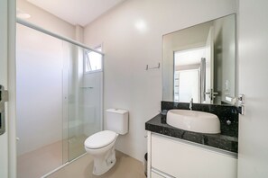 Une salle de bain moderne avec une douche à l’italienne en verre, des toilettes blanches et un meuble-lavabo doté d’un grand miroir.