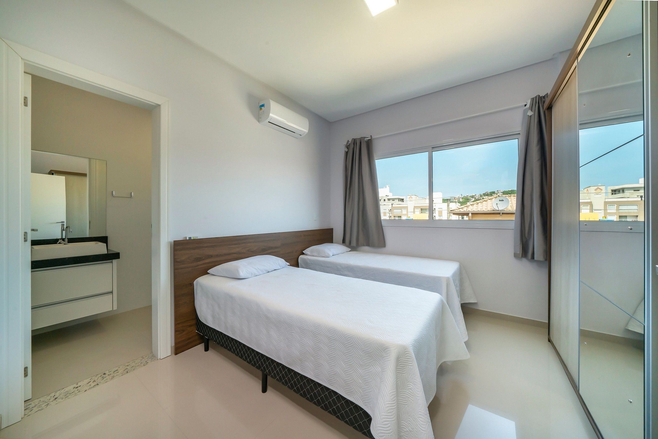 A hotel room with two beds, a bathroom with a mirror, and a window with curtains.