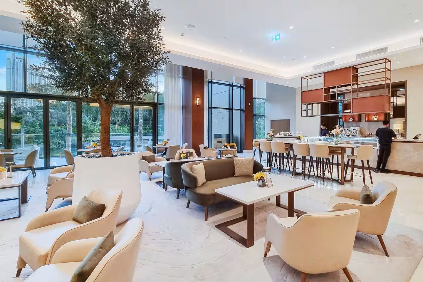 Eine moderne Hotelhalle mit einer großen Zimmerpflanze, gemütlicher Sitzgelegenheiten, einer Bar und großen Fenstern mit Blick auf die Stadt.