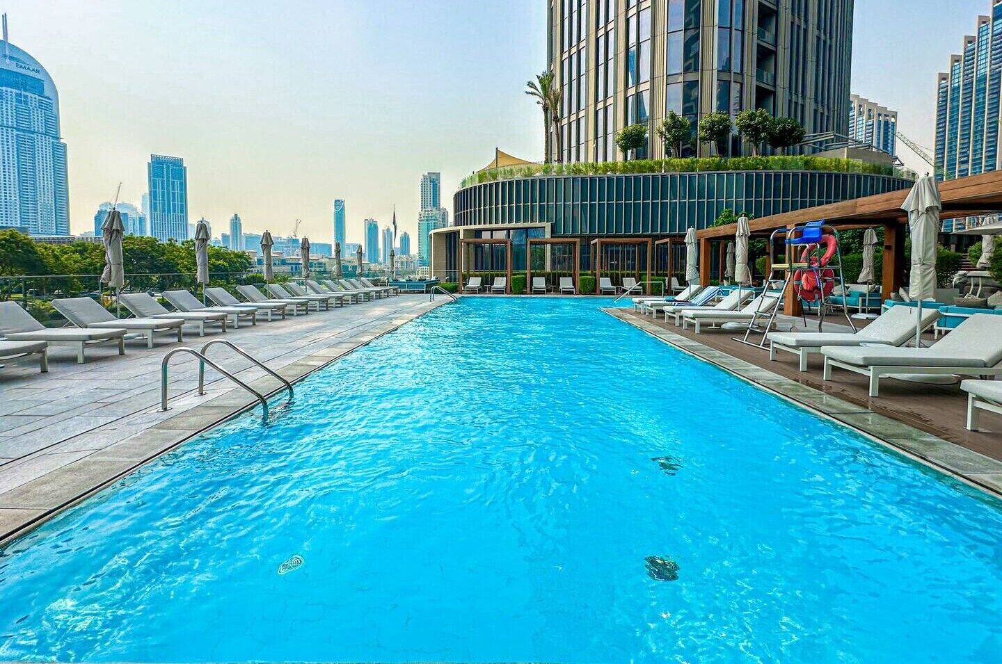 Ein Swimmingpool mit Liegestühlen und Sonnenschirmen, umgeben von modernen Gebäuden.