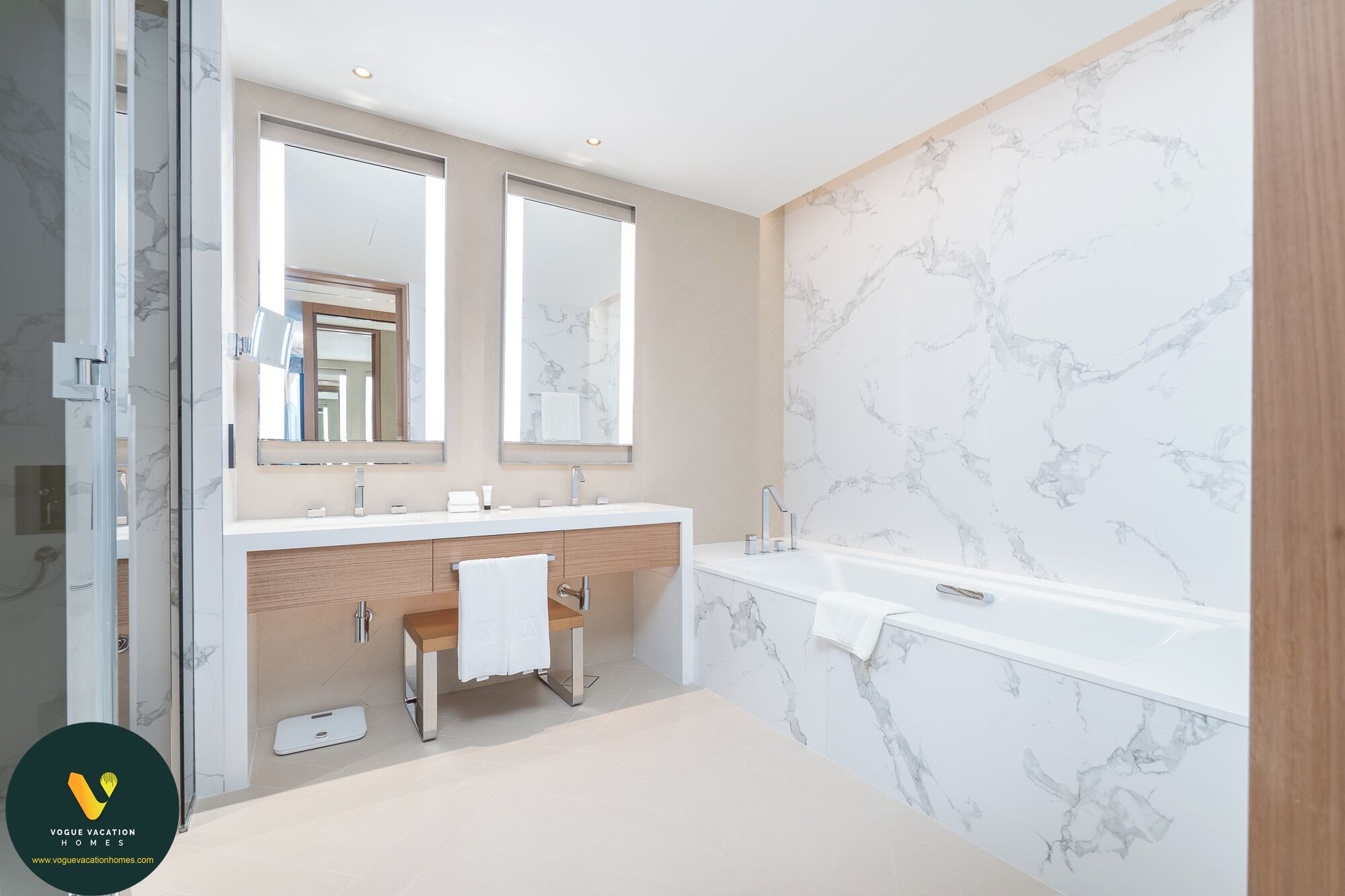 A modern bathroom with a marble backsplash, two sinks, a bench, and a large mirror.