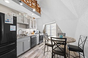 Et kompakt køkken med moderne hårde hvidevarer, et spiseområde med et marmorbord og et skråt loft.