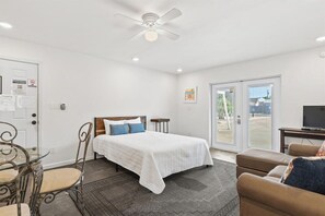A bedroom with a bed, a television, a dining table with chairs, a ceiling fan, and a sliding glass door leading to an outdoor area. - Short Walk To Beach | Additional Studio (Panama City Beach)