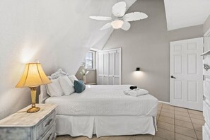 A bedroom with a bed, bedside lamp, ceiling fan, and a door.