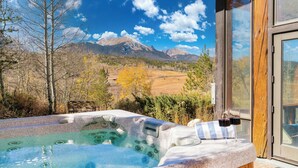 A hot tub with a mountain view, wooden deck, and a glass door leading to a covered area. - Topaz Estate by Avantstay Luxe Home, Pool + View (Silverthorne)