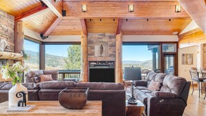 A spacious living area with a large sectional sofa, a wooden coffee table, and a stone fireplace. - Topaz Estate by Avantstay Luxe Home, Pool + View (Silverthorne)
