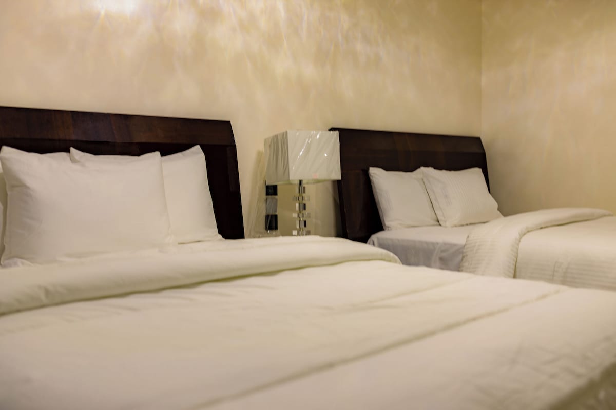 Una habitación de hotel con dos camas, una mesita de noche con lámpara y cabecera de madera.