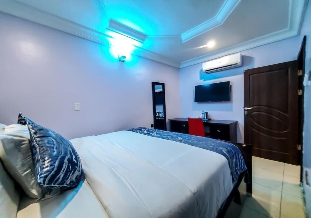 A hotel room with a bed, a desk, a TV, and an air conditioning unit.