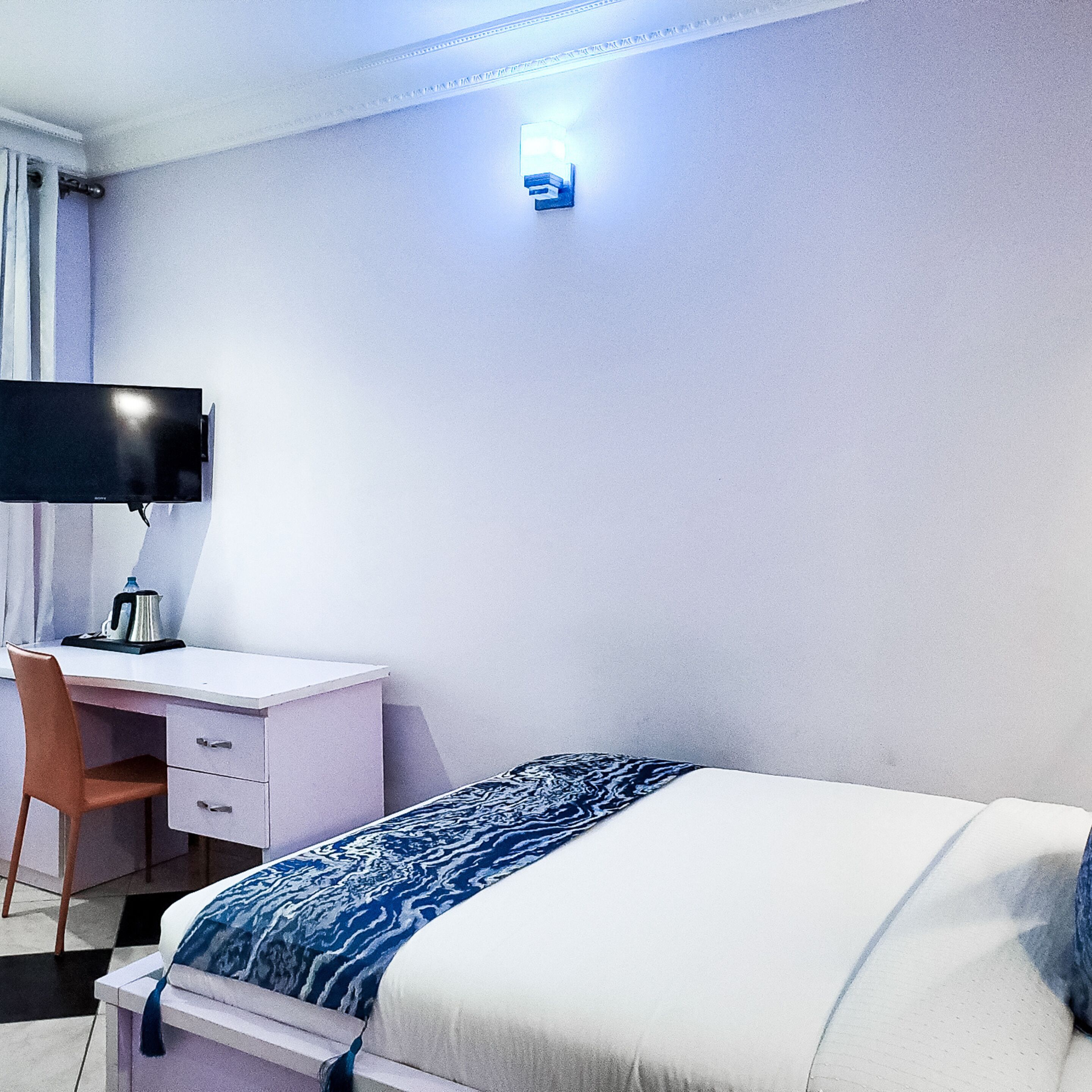 Hotelkamer met een bed, bureau met stoel, flatscreen televisie en een wandlamp.