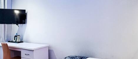 A hotel room with a bed, a desk with a chair, a flat-screen TV, and a wall-mounted light.