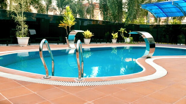 A swimming pool with a tiled edge, surrounded by potted plants and a blue canopy. - Hotel Medallion (Lekki)