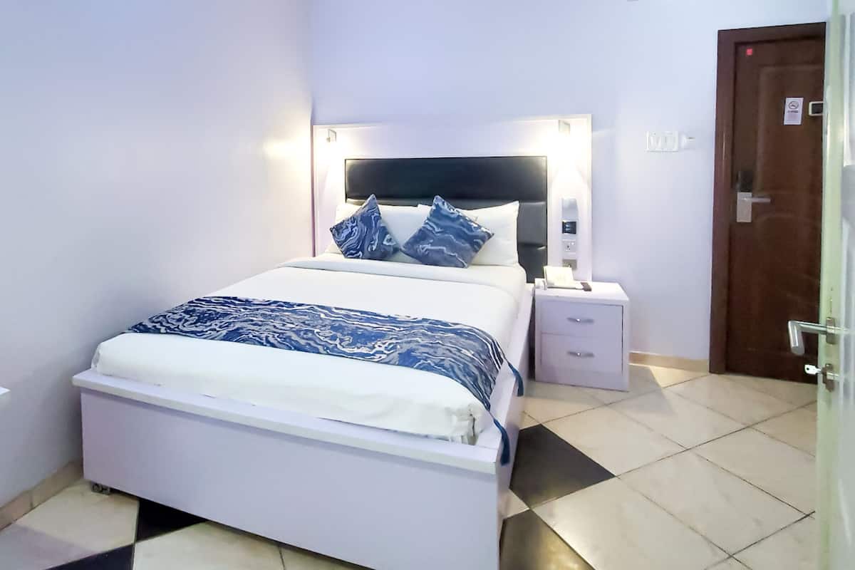 A bedroom with a bed, bedside tables, a nightstand, a door, and a light switch on the wall.