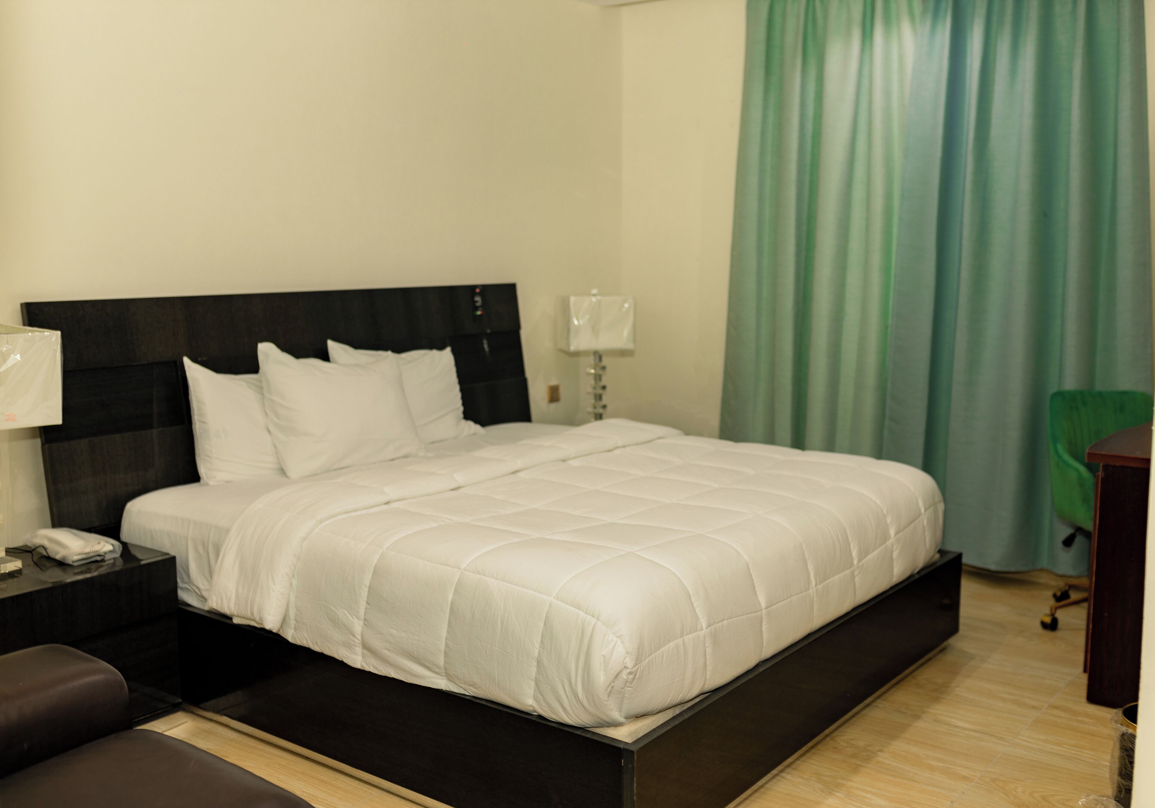A hotel room with a large bed, a bedside table, a lamp, and a green curtain.