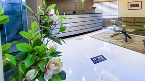 A reception area with a modern design, featuring a curved ceiling, a reception desk, a plant, and a sign on the floor. - Hotel Medallion (Lekki)