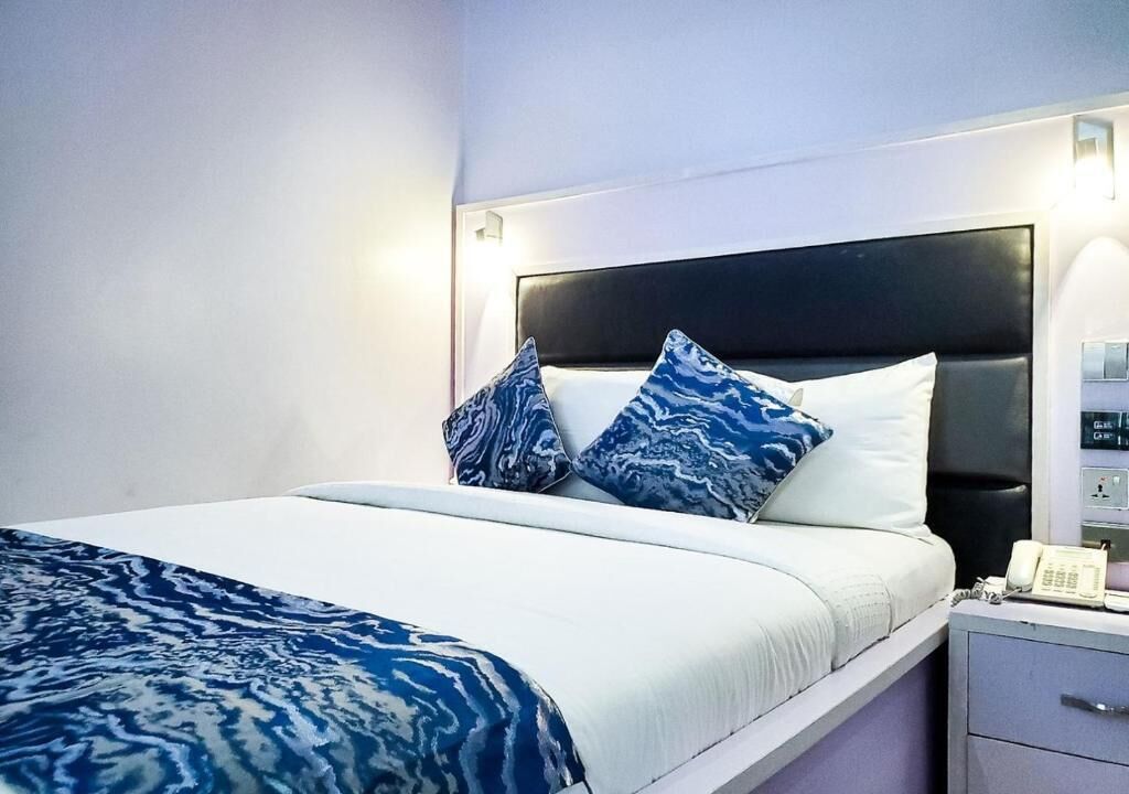 A neatly made bed with a white and blue patterned bedspread, two matching pillows, and a bedside table with a telephone.