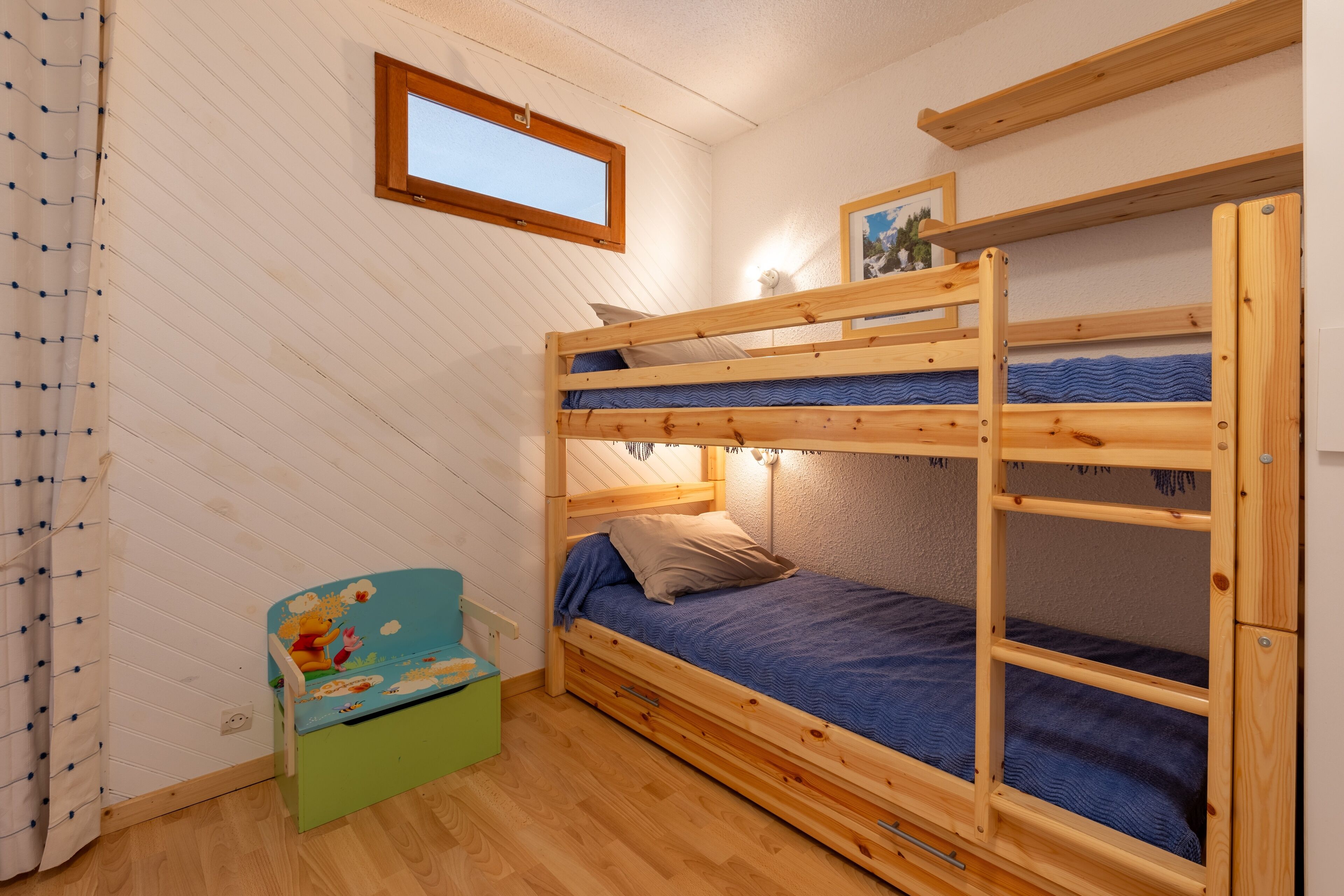 Une chambre avec un lit superposé, une fenêtre, un petit bureau et une chaise.