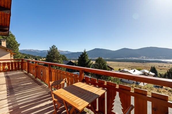 Eine Holzterrasse mit Tisch und Stühlen, mit Blick auf eine reizvolle Landschaft mit Bergen und einem See.