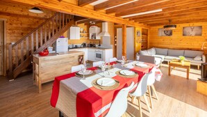 A wooden cabin interior with a dining area, kitchen, and living space.