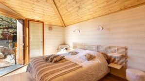 A wooden cabin bedroom with a bed, a chair, and a small table.