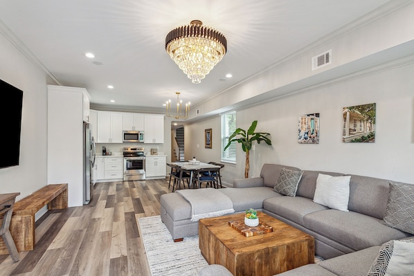 A modern living room with a grey sofa, wooden coffee table, and a chandelier.