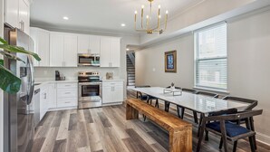 Une cuisine moderne avec des meubles blancs, des appareils en acier inoxydable, un banc en bois et une table à manger avec des chaises.