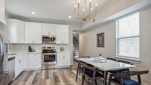 Una cocina moderna con armarios blancos, electrodomésticos de acero inoxidable y un comedor con mesa de vidrio y sillas de madera.