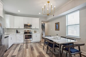 Una cocina moderna con armarios blancos, electrodomésticos de acero inoxidable y un comedor con mesa de vidrio y sillas de madera.
