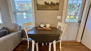 Uma sala de jantar com uma mesa de madeira escura, cadeiras brancas, um relógio e um castiçal.