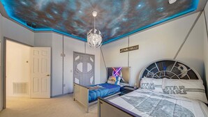 Un dormitorio con techo decorado con motivos galácticos, una cama y un póster de Star Wars.