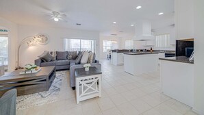 Una cocina moderna con armarios blancos, una isla central y un área de comedor con un sofá gris y una mesita de centro.