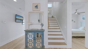 Un intérieur moderne avec un escalier en bois, un meuble bleu orné d’une pancarte de bienvenue et un tableau encadré accroché au mur.