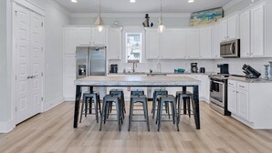 A modern kitchen with white cabinetry, a large island with bar stools, stainless steel appliances, and pendant lighting. - Beach Haven: Free golf cart, 2min to beach, Heated pool, Private backyard (Miramar Beach)