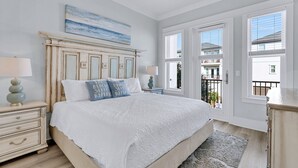 A bedroom with a large bed, two bedside tables, a ceiling fan, and a view of the outside balcony. - Beach Haven: Free golf cart, 2min to beach, Heated pool, Private backyard (Miramar Beach)