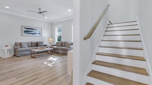 A modern living room with a grey sofa, a coffee table, and a staircase with wooden steps. - Beach Haven: Free golf cart, 2min to beach, Heated pool, Private backyard (Miramar Beach)