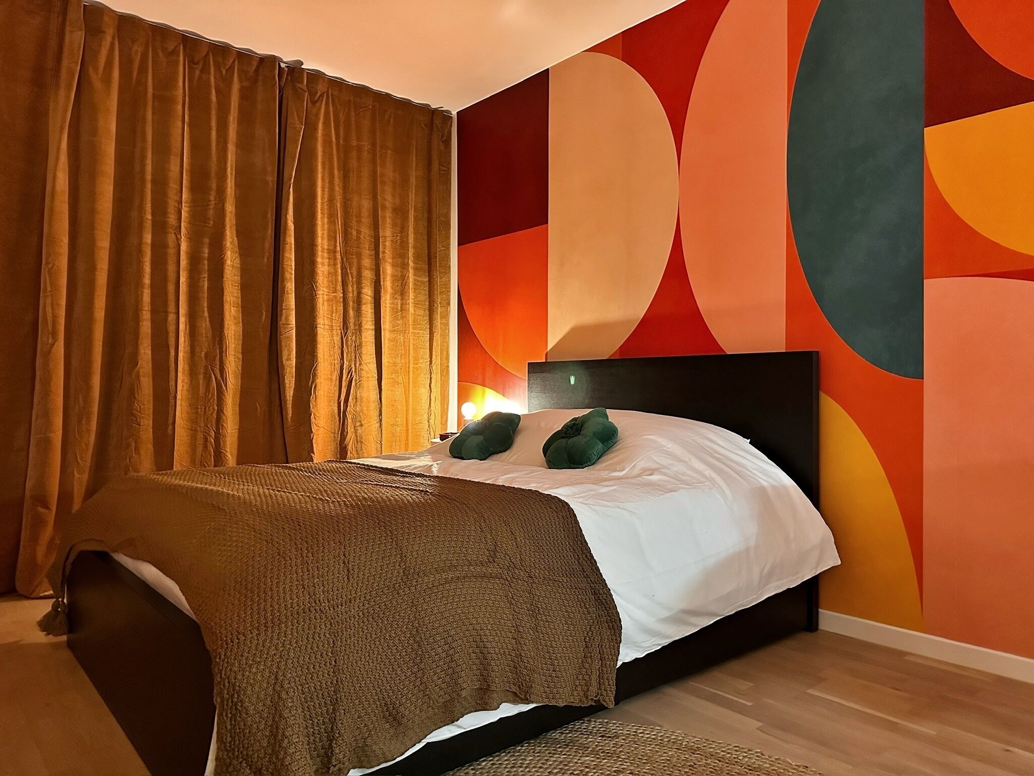 A bedroom with a bed, a headboard, a nightstand, a lamp, and a wall with abstract art.
