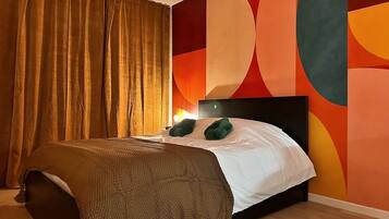 A bedroom with a bed, a headboard, a nightstand, a lamp, and a wall with abstract art.