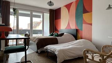 A modern bedroom with a bed, a chair, a table, and a large window.