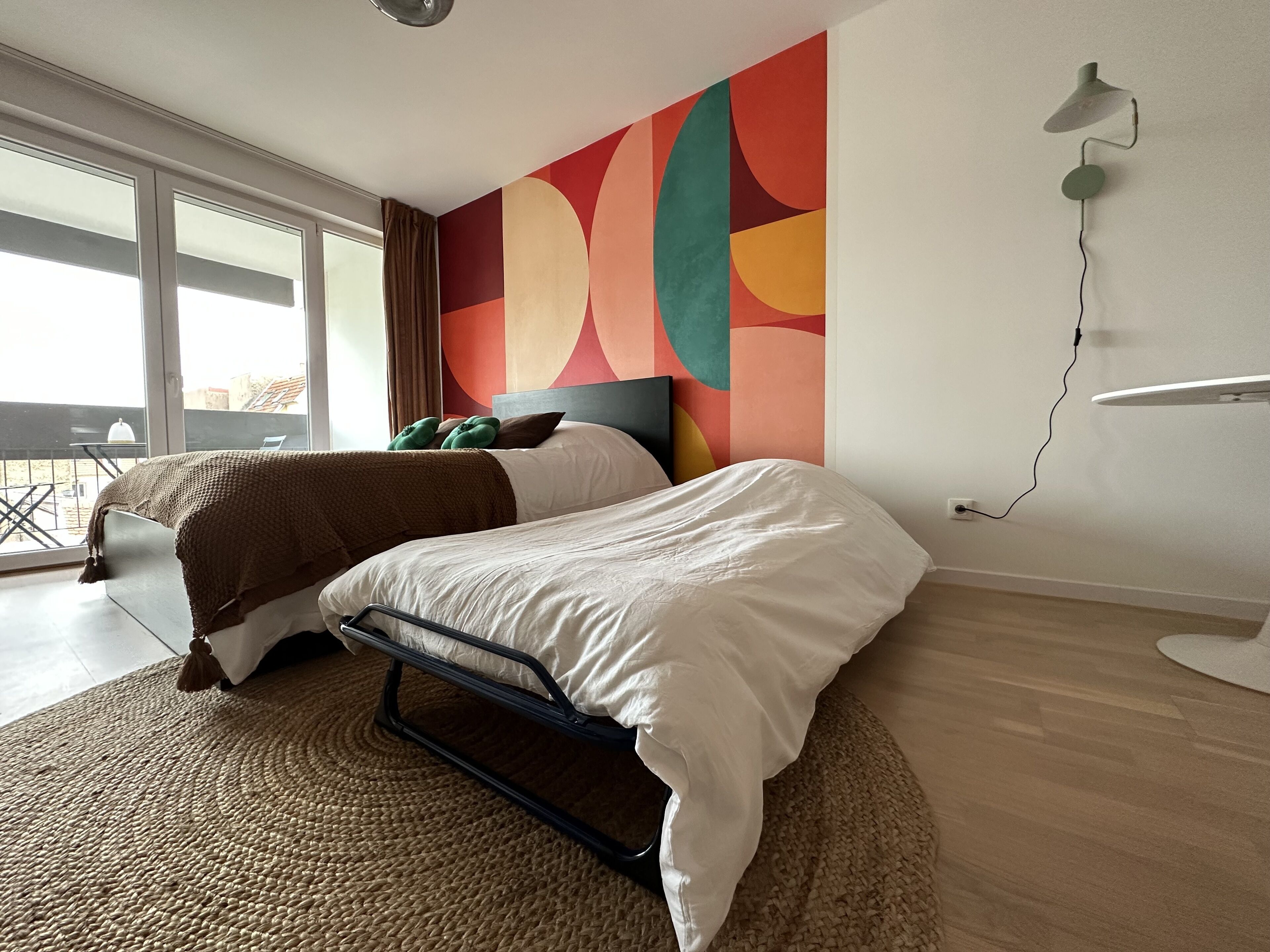 A modern hotel room with a large bed, a view of the city, and a colorful abstract wall art.