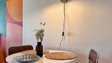 A dining area with a round table, two chairs, a vase with dried flowers, and a modern floor lamp.