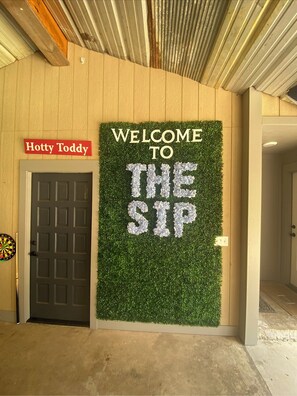 A welcome sign with "WELCOME TO THE SIP" on a green wall, a door labeled "Hotty Toddy," and a dartboard on the wall. - Welcome to the Sip! 7 bed 9 bath party house. Create your own grove party!  (Oxford)