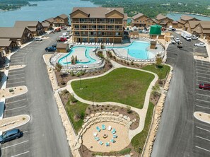 A hotel with a swimming pool, a parking lot, and a landscaped area with lounge chairs.